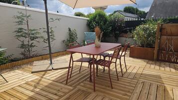 A wooden deck with a red table and chairs, an umbrella, and potted plants.