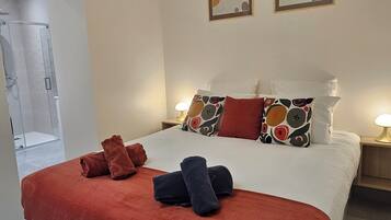 A hotel room with a bed, two pillows, a nightstand, a lamp, and a shower area.