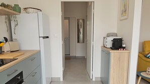 A modern kitchen with a refrigerator, oven, and microwave. There is a wooden countertop with a sink and a small table with a kettle and cups. A door leads to a hallway and another room. - Vineyard and Chateau Stay Vouvray (Vouvray)