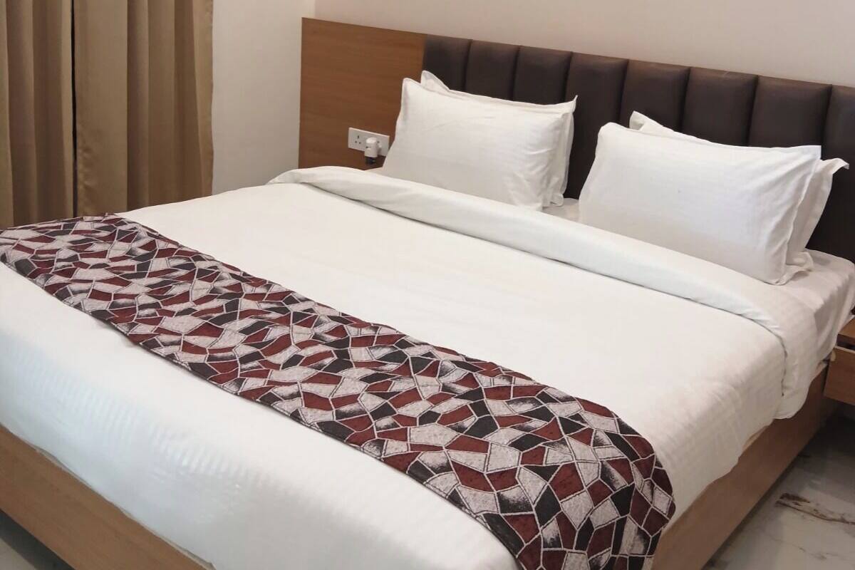 A neatly made double bed with a patterned throw blanket, a wooden headboard, and a bedside table with a lamp.