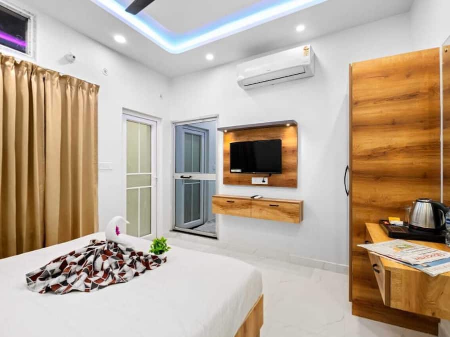 A modern hotel room with a bed, a wooden desk, a television, and a window with curtains.