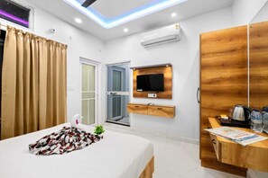 A modern hotel room with a bed, a wooden desk, a television, and a window with curtains. - Hotel Maa Vaishno (Ayodhya)