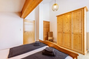 A room with a bed, a wooden wardrobe, a chair, and a hanging light fixture.