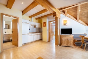 A spacious kitchen with wooden beams, a dining area with a TV, and a cozy seating arrangement.