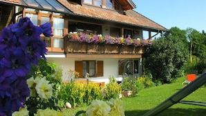 A two-story house with a sloped roof, large windows, and a balcony with flower boxes.