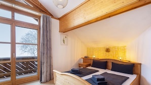 A bedroom with a wooden bed, a nightstand, a window with curtains, and a wall-mounted lamp.