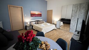 A modern bedroom with a bed, bedside tables, a mirror, and a dining area with a table set for two. - HOME Joséphine, a stone's throw from the Palace, Garden,parking,Kitchen, (Caserta)