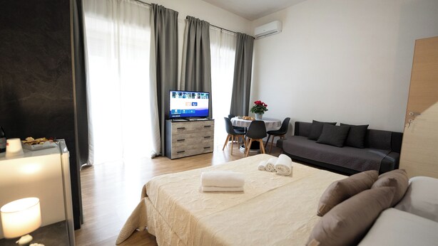 A modern hotel room with a bed, a desk, a television, and a sofa. - HOME Joséphine, a stone's throw from the Palace, Garden,parking,Kitchen, (Caserta)