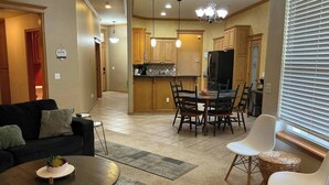 A living room with a sofa, coffee table, and chairs, a dining area with a table and chairs, and a kitchen with wooden cabinets and a TV. - Del City 6 Bed 2.5 Bath-Sleeps 14!, The Gathering-Spacious 6 Bedroom (Del City)