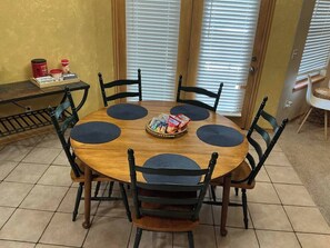 A round wooden table with six chairs, a tray of snacks, and a coffee maker on a table against a yellow wall with a window in the background. - Del City 6 Bed 2.5 Bath-Sleeps 14!, The Gathering-Spacious 6 Bedroom (Del City)