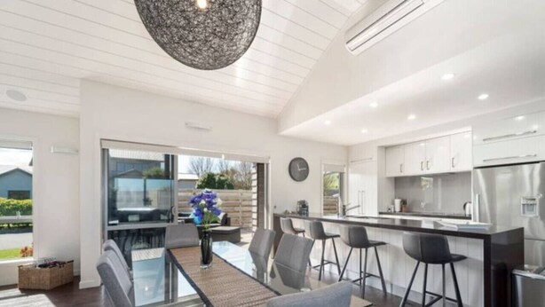 Een moderne keuken met een centraal eiland, barkrukken en een eetgedeelte met een glazen tafel.