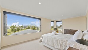 Un dormitorio con un ventanal grande, una cama, una silla y una mesita de noche.