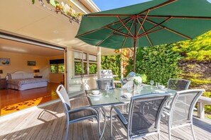 An outdoor dining area with a table set for four, surrounded by chairs, under a green umbrella.
