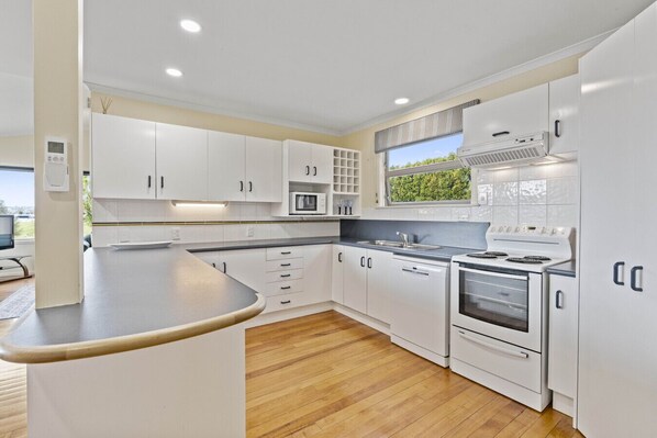 A modern kitchen with white cabinets, a built-in oven, microwave, and a large window providing natural light.