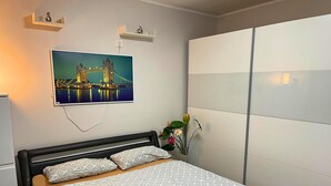Un dormitori amb un llit, un quadre d'un pont, un armari i una petita planta.