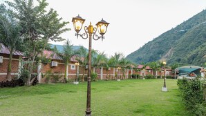 A courtyard with a lamp post, brick buildings, and a mountain in the background. - Kwality Beach Resort (Purano Jhangajholi)