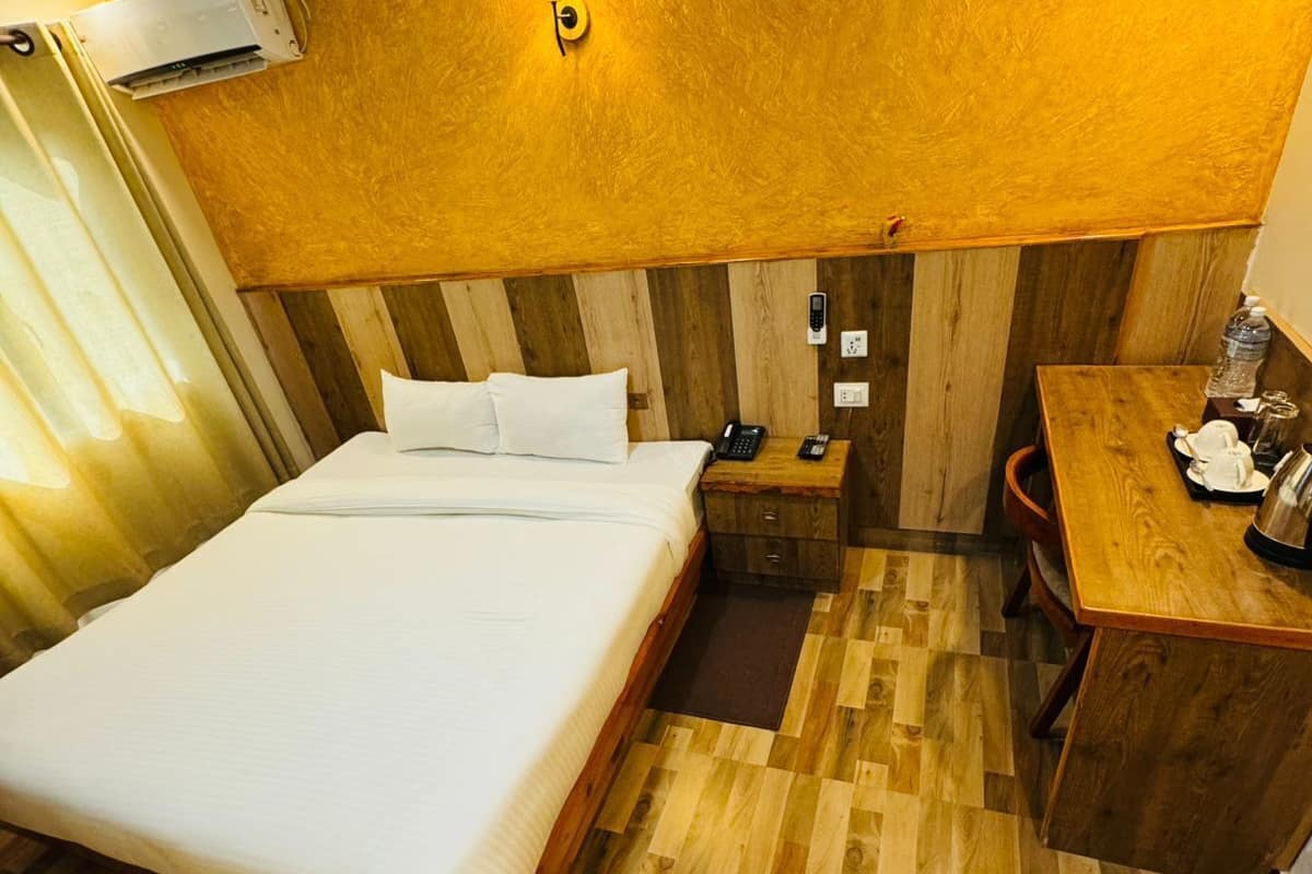 Ein Hotelzimmer mit Holzboden, einem Bett mit weißer Bettwäsche, einem Nachttisch mit Lampe und einem kleinen Schreibtisch mit Stuhl.