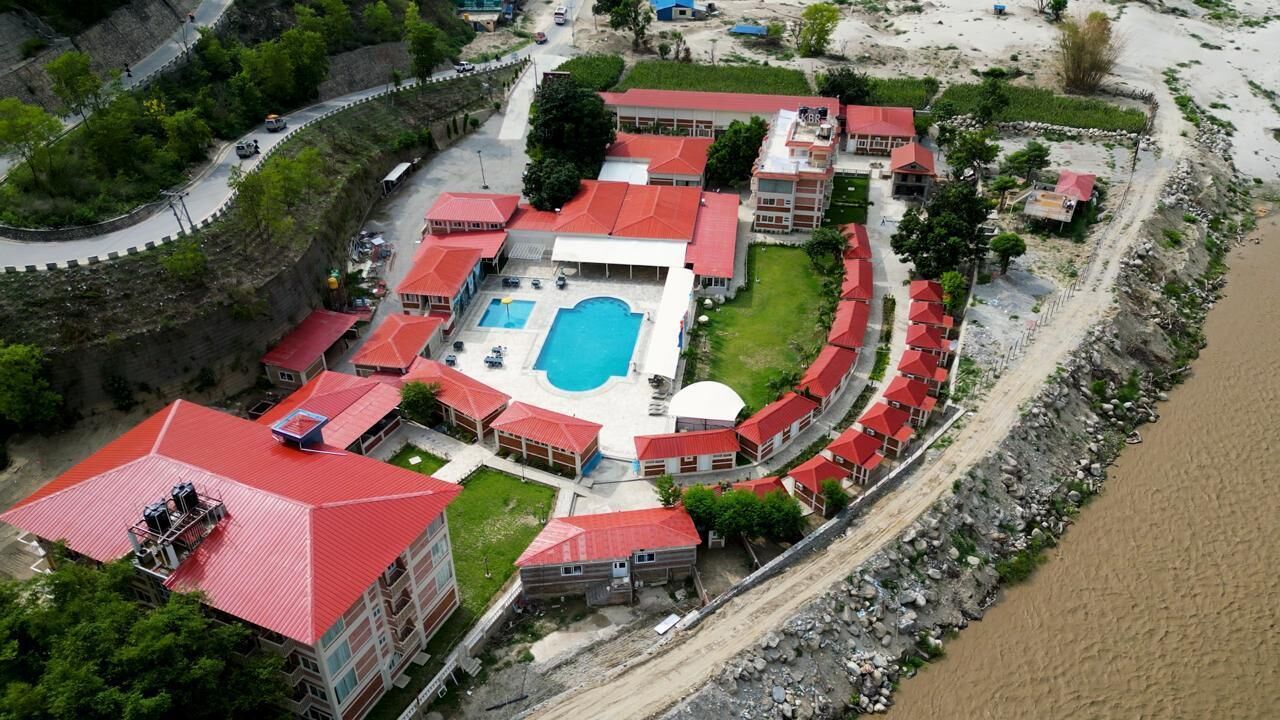 Vista aérea de un complejo turístico con piscina, varias edificaciones de techo rojo y un río.