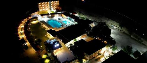An aerial view of a hotel with a swimming pool, multiple guest rooms, and a well-lit outdoor area.