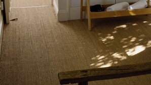 Ein Zimmer mit einer hölzernen Sitzbank, einem Kleiderständer mit Kleiderbügeln und einer Tür zu einem weiteren Raum.