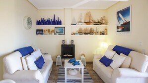 Een woonkamer met twee witte banken, een salontafel in het midden en een open haard. Er staan planken met decoratieve objecten en een poster aan de muur.