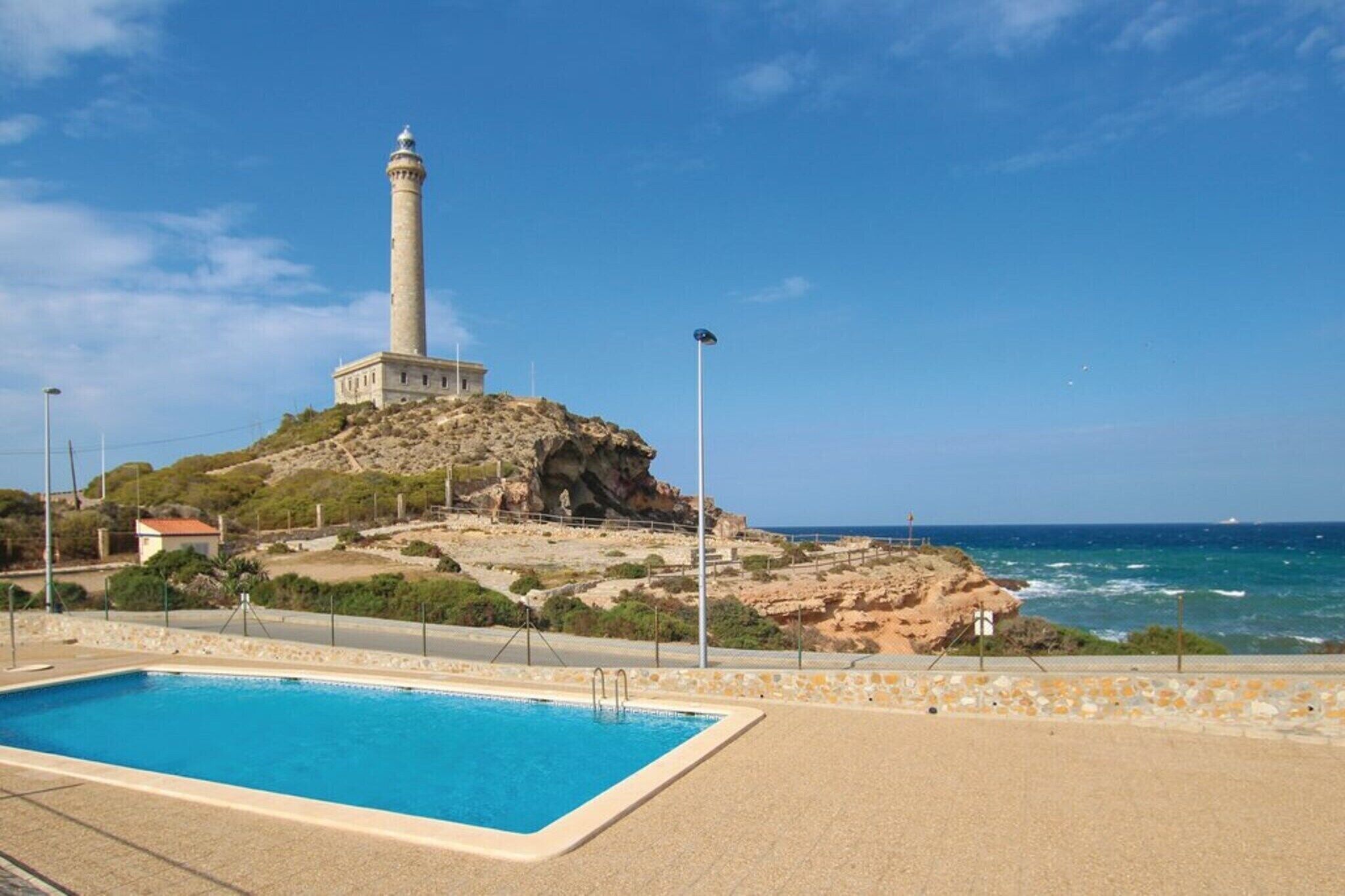 Una piscina, un faro y un litoral rocoso con el océano al fondo.