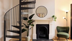 A modern interior with a spiral staircase, a fireplace, a green armchair, and a potted plant.