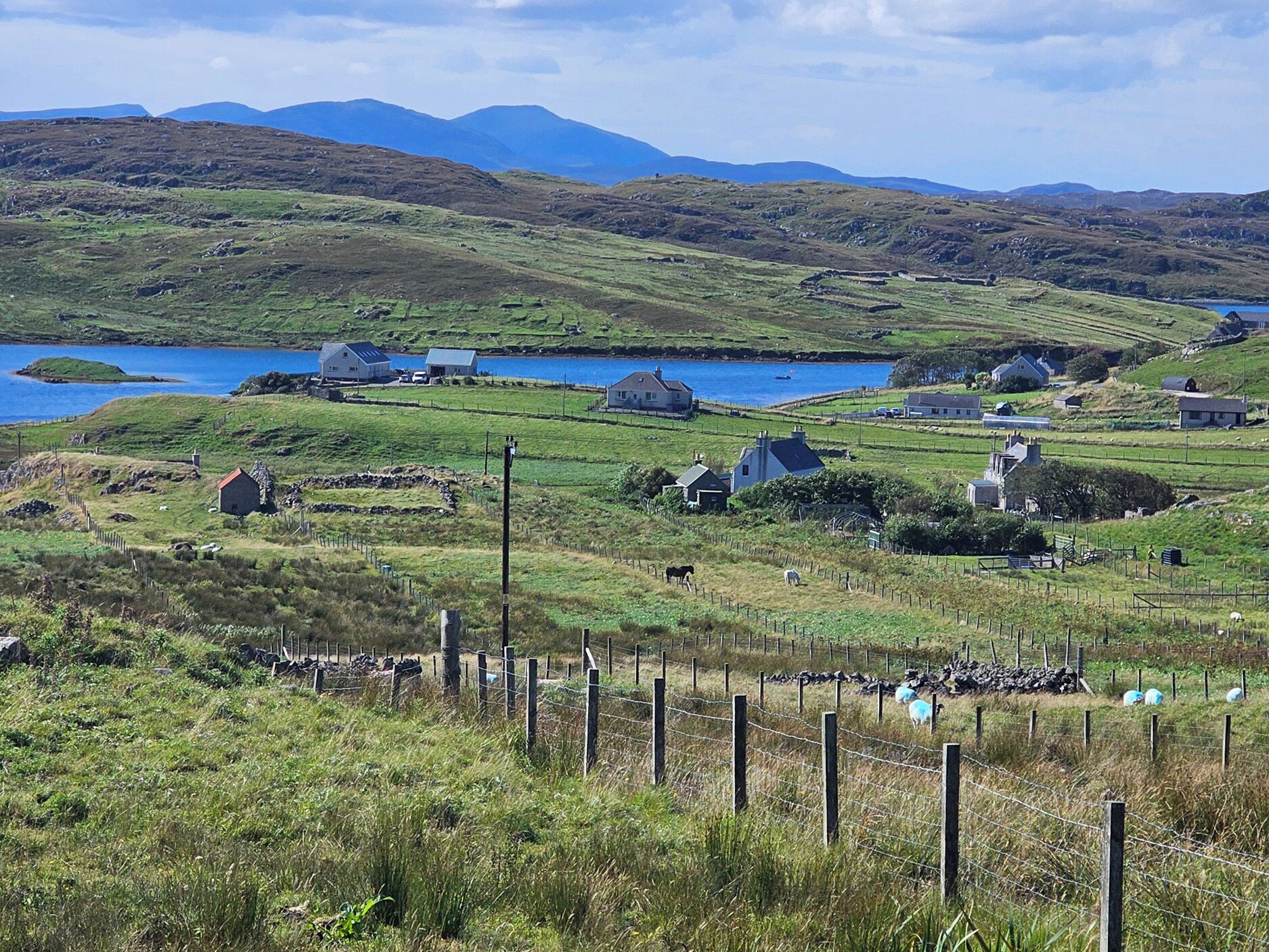 A rural landscape with houses, a lake, and mountains in the background.
