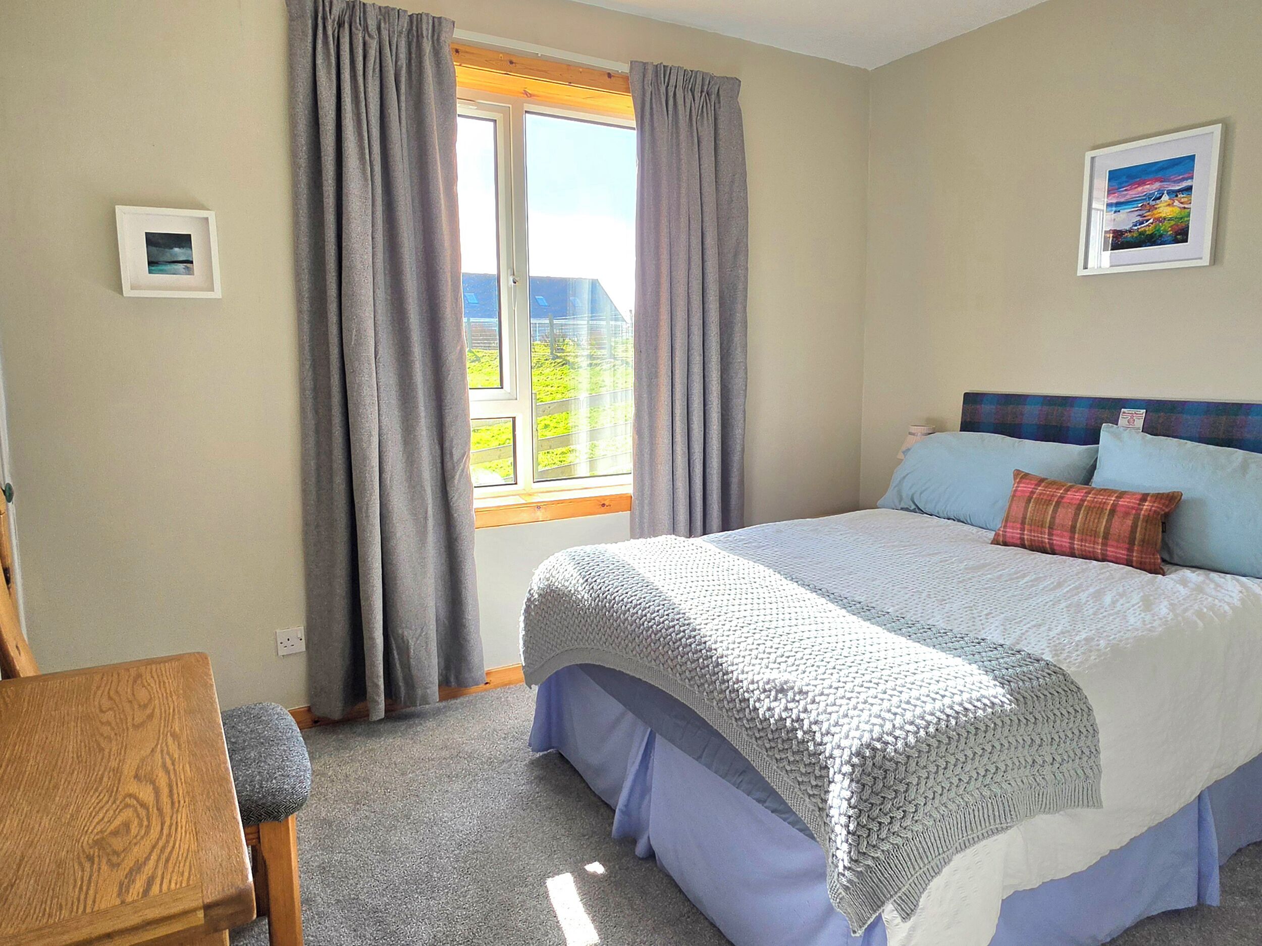 A bedroom with a large bed, a wooden chair, a window with curtains, and a framed picture on the wall.