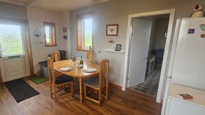 Zona de menjador amb taula i cadires de fusta, nevera i una porta que condueix a una altra habitació.
