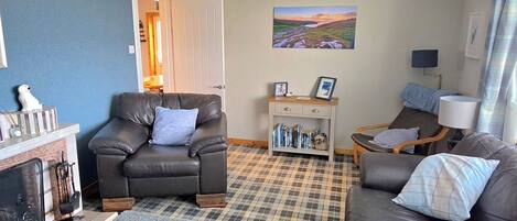 Una sala de estar con chimenea, un sofá, un sillón, una mesita con libros y un cuadro en la pared.