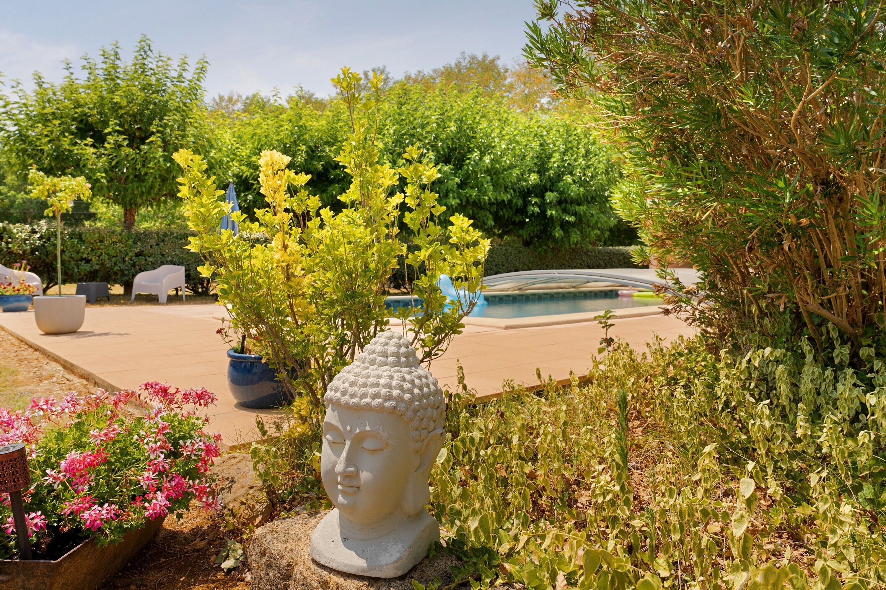 A garden with a Buddha statue, potted plants, and a pool in the background.