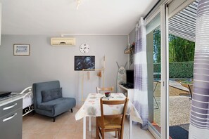 A compact living space with a kitchenette, a sofa, a dining table with chairs, a TV, and a view of the outdoors. - Studio with Shared Pool, Wi-Fi, and Air Conditioning (Montayral)