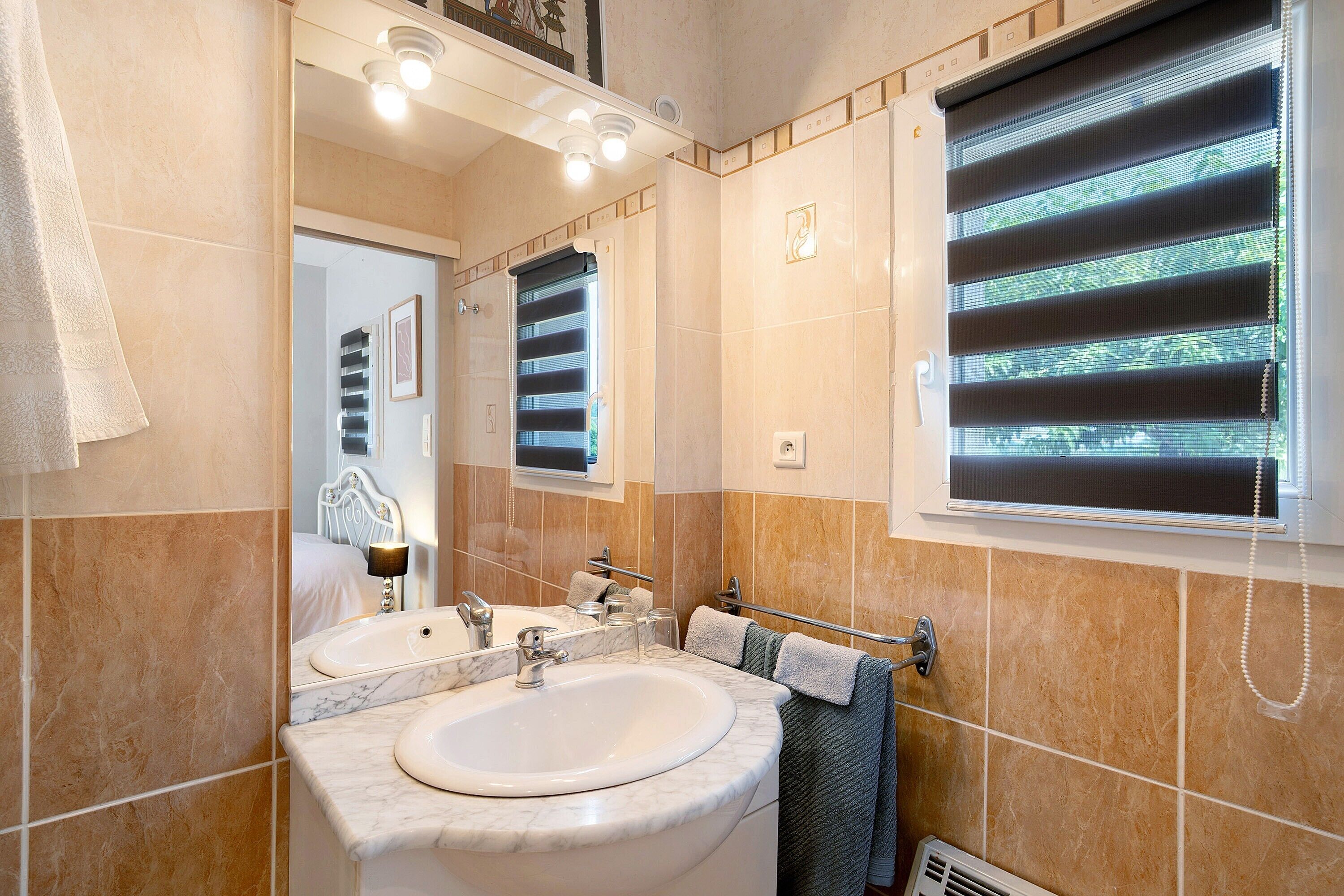 Une salle de bain avec deux lavabos, un miroir, un porte-serviettes et une fenêtre avec des stores.
