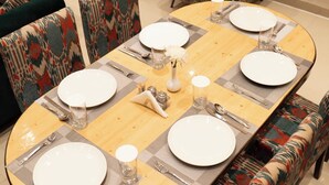 Una mesa de comedor dispuesta con platos blancos, cubiertos y vasos, rodeada de sillas tapizadas con estampado.