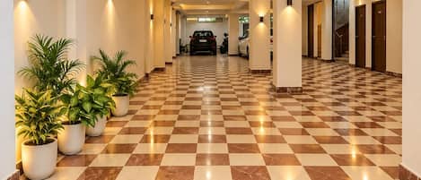 A hotel corridor with checkered flooring, potted plants, and doors on the right.