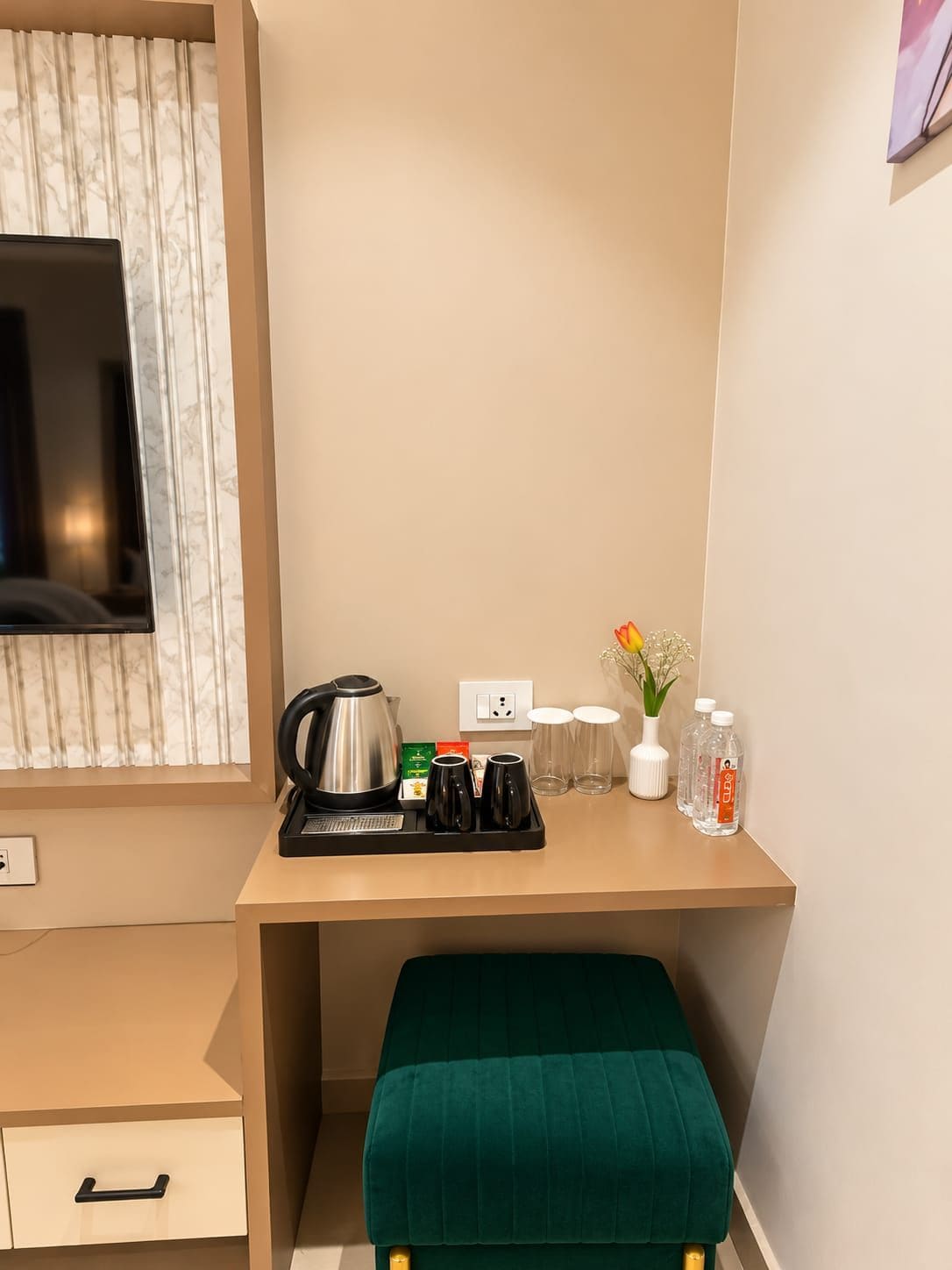 Una habitación de hotel con una cama, un escritorio con una tetera, tazas y un florero con flores.