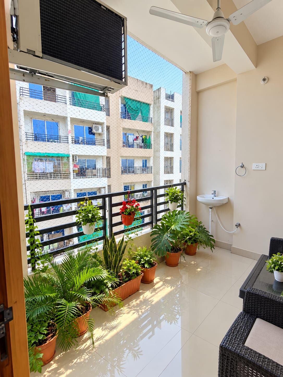 A balcony with potted plants, a ceiling fan, and a view of a building with balconies.