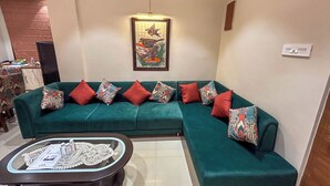 Un sofá color turquesa con cojines estampados, una mesa de centro de vidrio con un tablero decorativo, y una obra de arte enmarcada sobre el sofá.