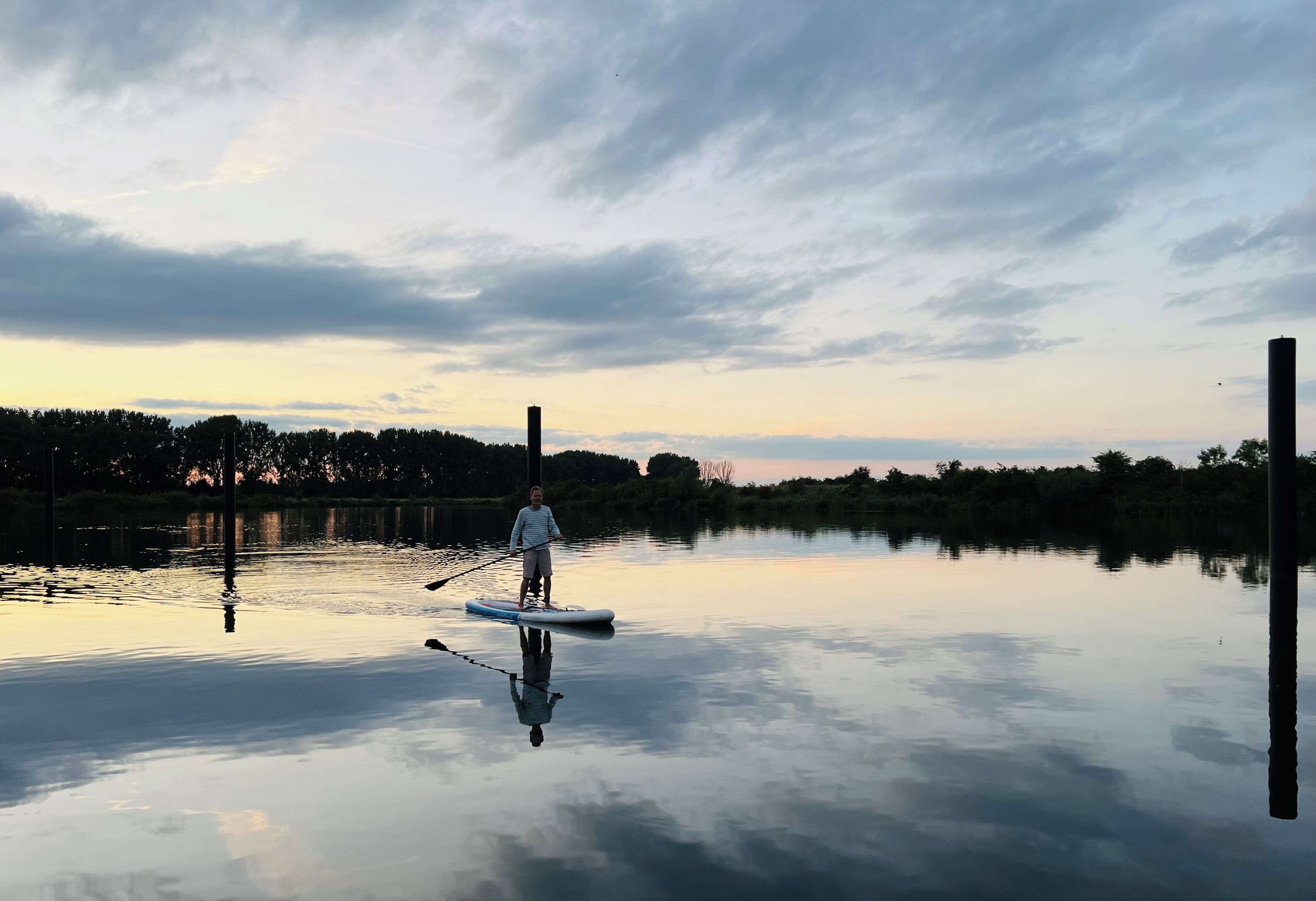 Una persona haciendo paddleboard en aguas tranquilas, con una orilla boscosa al fondo.