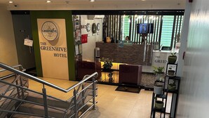 Zona de recepción de un hotel, con mostrador de recepción, señalización de área restringida y una escalera que sube a un piso superior.