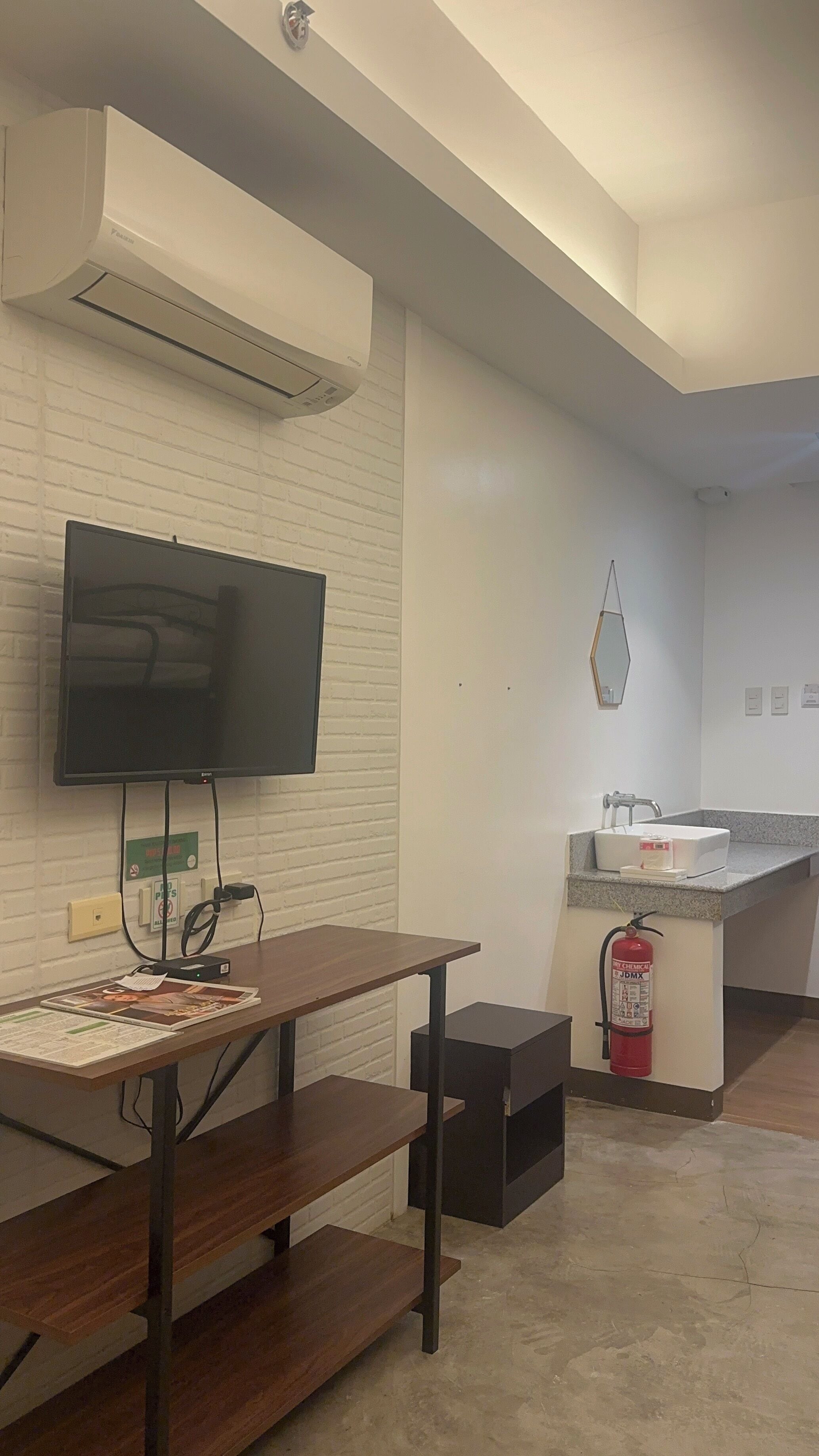 A modern kitchen with a built-in sink, a fire extinguisher, and a flat-screen TV mounted on a brick wall.