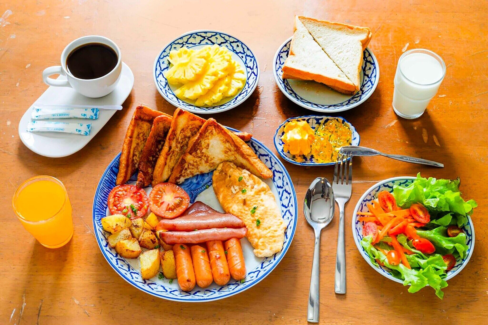 Ein Frühstückstisch mit Toast, Eiern, Würstchen, Tomaten und einem Salat.