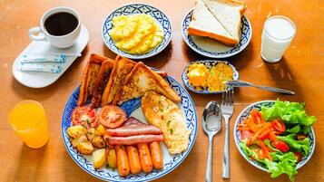 Ein Frühstückstisch mit Toast, Eiern, Würstchen, Tomaten und einem Salat.