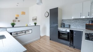 A modern kitchen with a built-in oven, a microwave, and a coffee maker. There is a clock on the wall and a plant on the counter. - Fife coastal corner (Buckhaven)