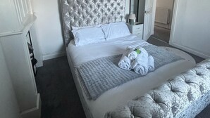 A neatly made bed with a tufted headboard, a bedside table with a lamp, and a door leading to another room. - Fife coastal corner (Buckhaven)