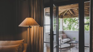 Een kamer met een bank, een lamp en uitzicht op een terras met een tafel en stoelen.