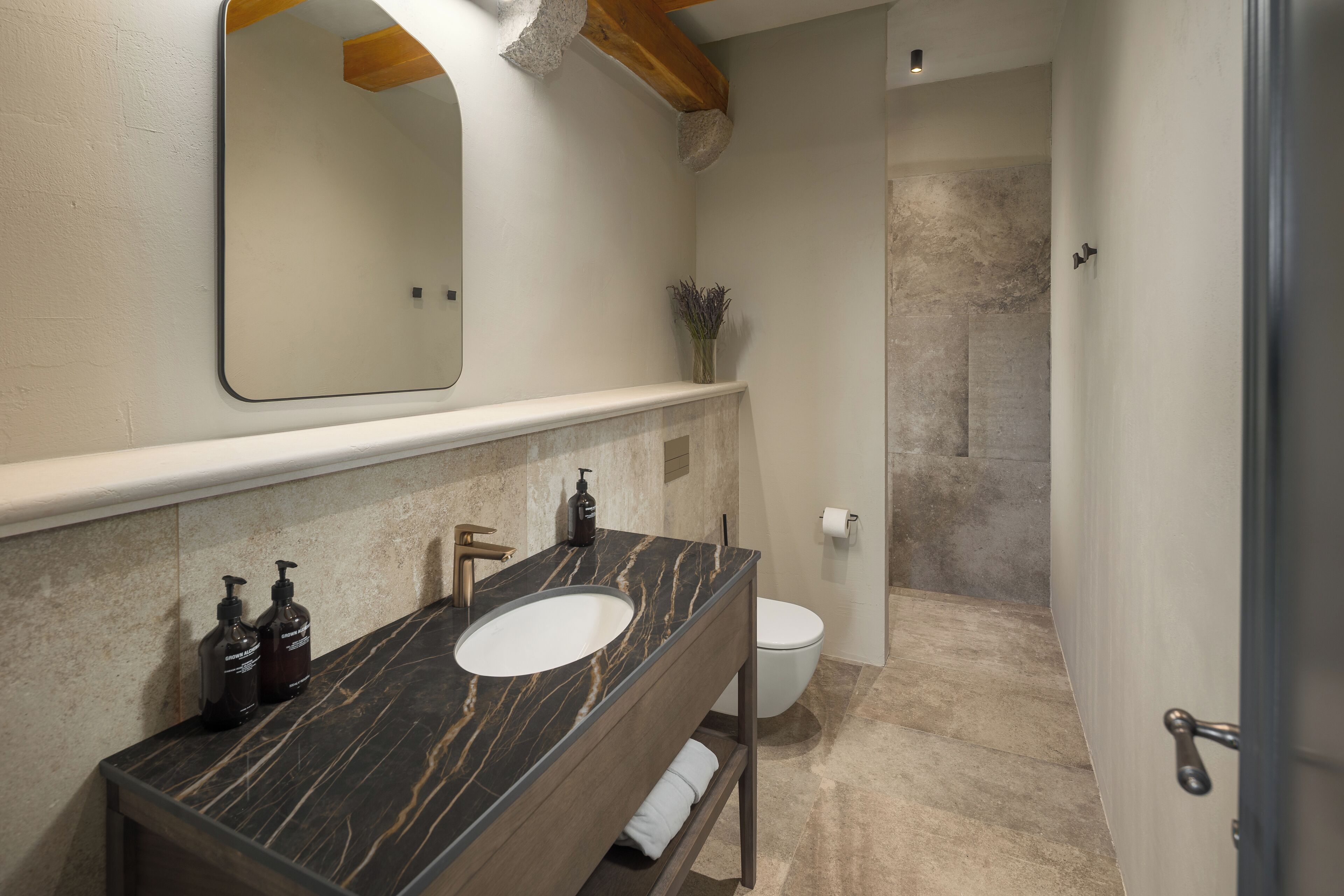 Une salle de bain avec un lavabo en marbre, un meuble-lavabo en bois, un miroir, des toilettes et un espace douche.