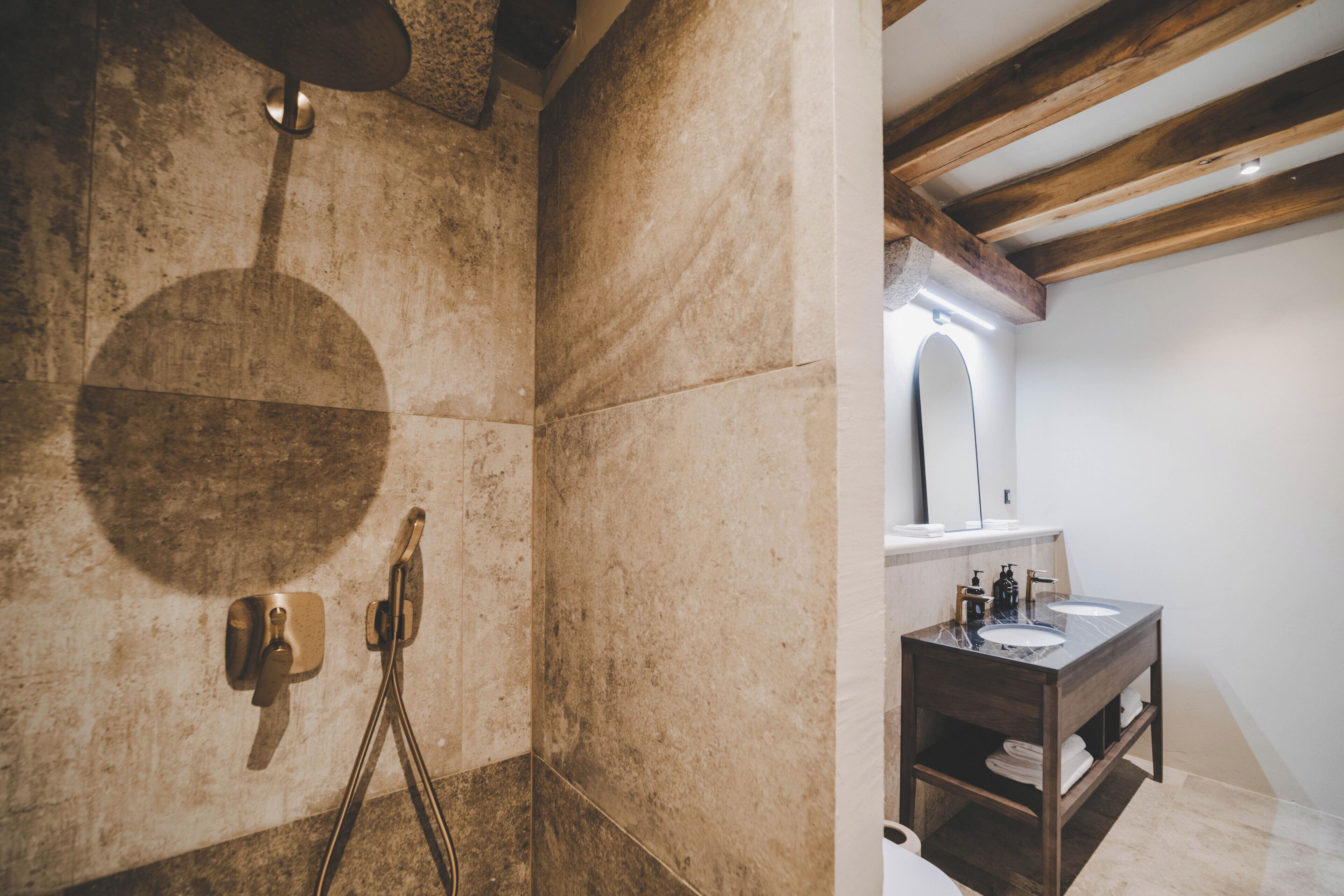 Un baño con pared de piedra, techo de madera, un lavamanos y un espejo.
