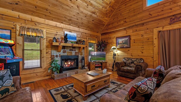 A cozy log cabin interior with a fireplace, wooden walls, a television, and a comfortable seating area. - Free Dollywood Tix/HotTub/Dog Friendly/A+ Location (Sevierville)